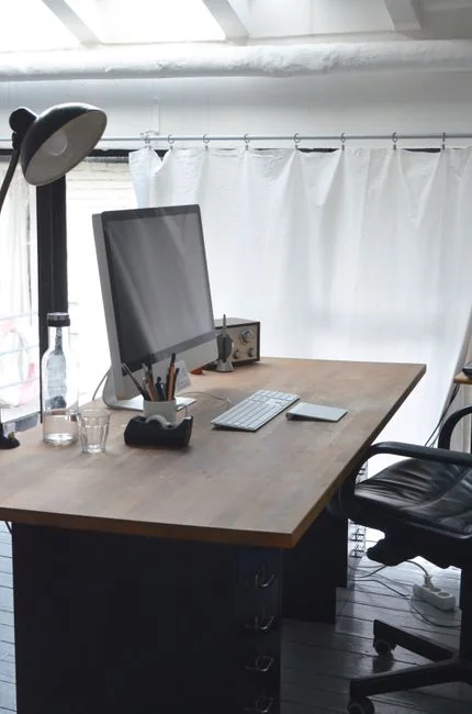 From an overhead view, a faceless person is using a mobile phone while working at a white marble table at home, with gadgets, a pen, and a pencil nearby